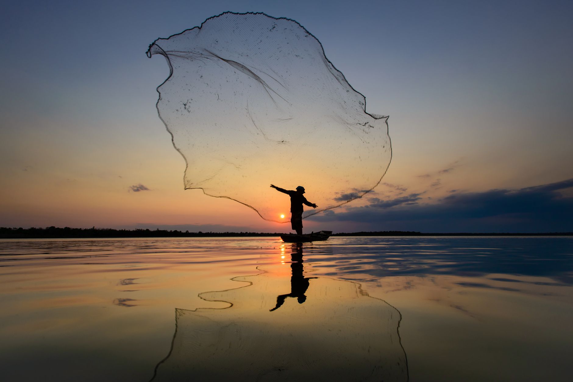 silhouette of man throwing fishnet while standing on a boat in the body of water